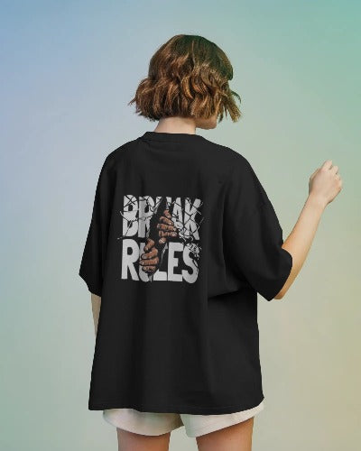 Back view of a woman wearing a black oversized t-shirt and light shorts against a pastel gradient backdrop. The large back graphic features a stylized basketball design with the text "BIG GAME RULES" on it.