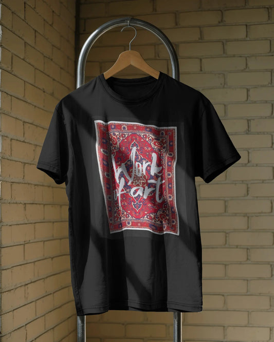 Framed in Threads: Work of Art Loose Fit Cotton Tee - A black loose fit cotton t-shirt is shown hanging on a wooden hanger against a background of a brick wall. The front of the shirt displays the large, square graphic that resembles a red and white framed rug design with the text "Work of Art" inside.
